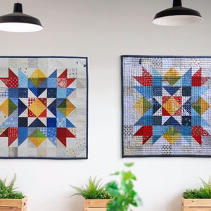 May include: Two colorful patchwork quilts with a starburst design in shades of blue, red, yellow, and green, hanging on a white wall.