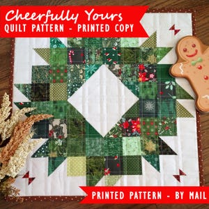 Puede incluir: Un patrón de acolchado impreso para una colcha con temática navideña. El patrón presenta un diseño de corona con una variedad de telas verdes, rojas y blancas. El título del patrón es "Cheerfully Yours - Printed Copy".