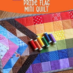 Peut inclure: Mini-couverture Pride Flag avec un motif patchwork aux couleurs de l'arc-en-ciel. La couverture présente des carrés et des triangles de différents motifs et couleurs, avec une bordure rayée noire et blanche. Dimensions finies : 45,7x30,5 cm. Plusieurs bobines de fil sont sur la couverture.