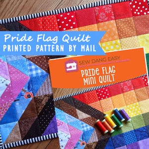 May include: A colorful Pride Flag mini quilt with a printed pattern. The quilt features a patchwork design with various fabrics in rainbow colors. The image also shows spools of thread and a book with the text "Pride Flag Mini Quilt".