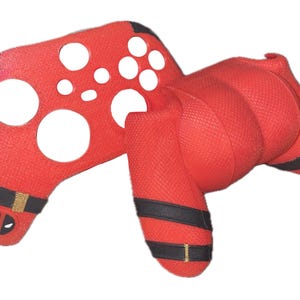 May include: Red and black silicone skin for a video game controller. The skin features a Deadpool character design.