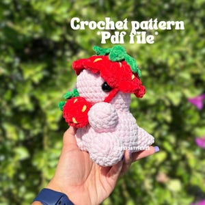 Puede incluir: Un juguete amigurumi de fresa de crochet rosa que lleva un sombrero de fresa rojo y verde. El juguete sostiene una fresa roja y verde en su mano. Patrón de crochet *Archivo Pdf*