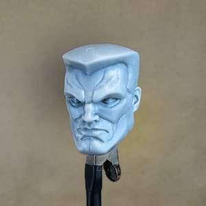 May include: An unpainted grey plastic head sculpt of a man with a serious expression. The head is mounted on a black stand.