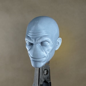May include: A 3D printed, light blue, bald head sculpture with a detailed face. The sculpture has a furrowed brow, closed eyes, and a slight smile.