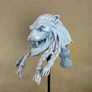 May include: A gray, 3D printed figurine of a lion's head with a braided mane and beard. The figurine is mounted on a black stand.