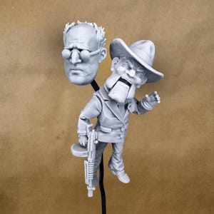 May include: A gray plastic figurine of a man wearing a hat and holding a gun. The figurine is standing on a black stand. There is a separate gray plastic head with glasses on a black stand.