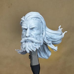May include: A 3D printed, unpainted, grey resin bust of a man with long hair and a beard. The hair is styled in a way that suggests it is blowing in the wind.
