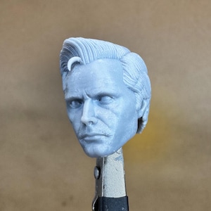 May include: A gray 3D printed head sculpt of a man with short, styled hair. The head is slightly tilted to the side, and the man has a serious expression on his face.
