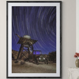 Könnte beinhalten: Ein gerahmtes Foto eines Oldtimers, der unter einem Turm mit einer Sternenspur am Nachthimmel geparkt ist. Das Foto hängt an einer Wand in einem Wohnzimmer mit einer Couch, einem Couchtisch und einem Stuhl.