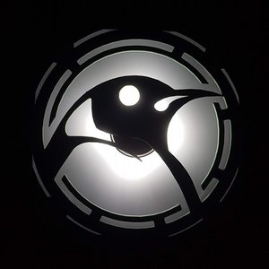 May include: A black silhouette of a bird with a white circle in the center, surrounded by a concentric circle design.