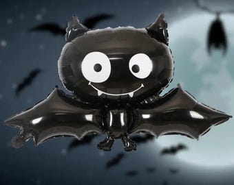 May include: Black balloon shaped like a bat with a smiling face and large white eyes. The bat has wings that are spread out.
