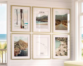 May include: Six framed art prints with gold frames are displayed on a white wall. The prints feature images of Hawaii, including a beach scene with a surfboard, a road through a forest, and a map of the islands.