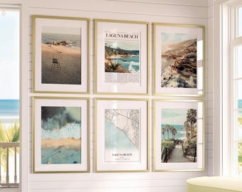 May include: Six framed art prints with gold frames are displayed on a white wall. The prints feature beach scenes, including a lifeguard chair, ocean waves, and a map. The text "LAGUNA BEACH" is visible on one print.