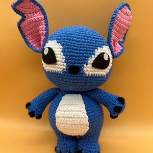 May include: A blue crocheted Stitch plush toy with pink ears, white fur on the belly, and black eyes.
