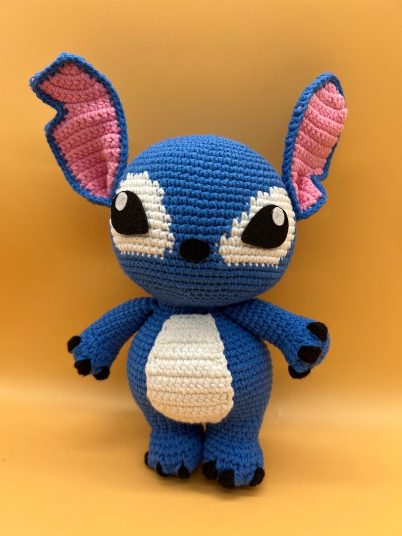 May include: A blue crocheted Stitch plush toy with pink ears, white fur on the belly, and black eyes.
