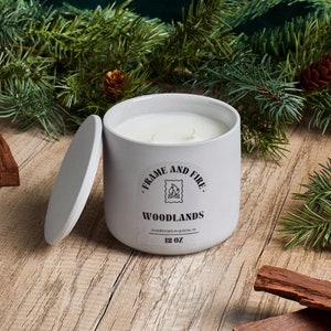 Frame and Fire luxury candles in ceramic jars with lids, featuring scents like Rosewood Lux, Saffron Noir, Cedarwood & Pine, Evergreen Fir, and Woodlands. Hand-poured coconut apricot wax candles styled with holiday decor, perfect for gifting or home