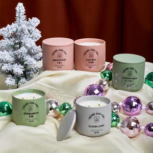 Frame and Fire luxury candles in ceramic jars with lids, featuring scents like Rosewood Lux, Saffron Noir, Cedarwood & Pine, Evergreen Fir, and Woodlands. Hand-poured coconut apricot wax candles styled with holiday decor, perfect for gifting or home