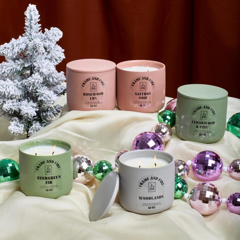 Frame and Fire luxury candles in ceramic jars with lids, featuring scents like Rosewood Lux, Saffron Noir, Cedarwood & Pine, Evergreen Fir, and Woodlands. Hand-poured coconut apricot wax candles styled with holiday decor, perfect for gifting or home