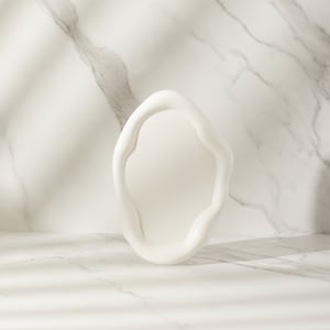 May include: White, abstract, organic-shaped frame on a white marble background. The frame is a modern, minimalist design and could be used for product photography or as a decorative element.