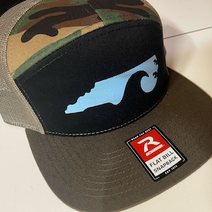 Może przedstawiać: Brązowa, czarna i kamuflażowa czapka typu snapback z płaskim daszkiem, z niebieskim obrysem Karoliny Północnej i falą z palmami z przodu. Czapka ma siateczkowe plecy i logo Richardson z boku. Tekst na logo brzmi "Wear the Best. Richardson. Flat Bill Snapback. Est. 1972."