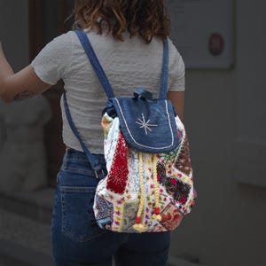 May include: A patchwork denim backpack with a drawstring closure and a star embroidered on the flap. The backpack is made of various fabrics in different colors and patterns, including red, white, blue, and yellow.