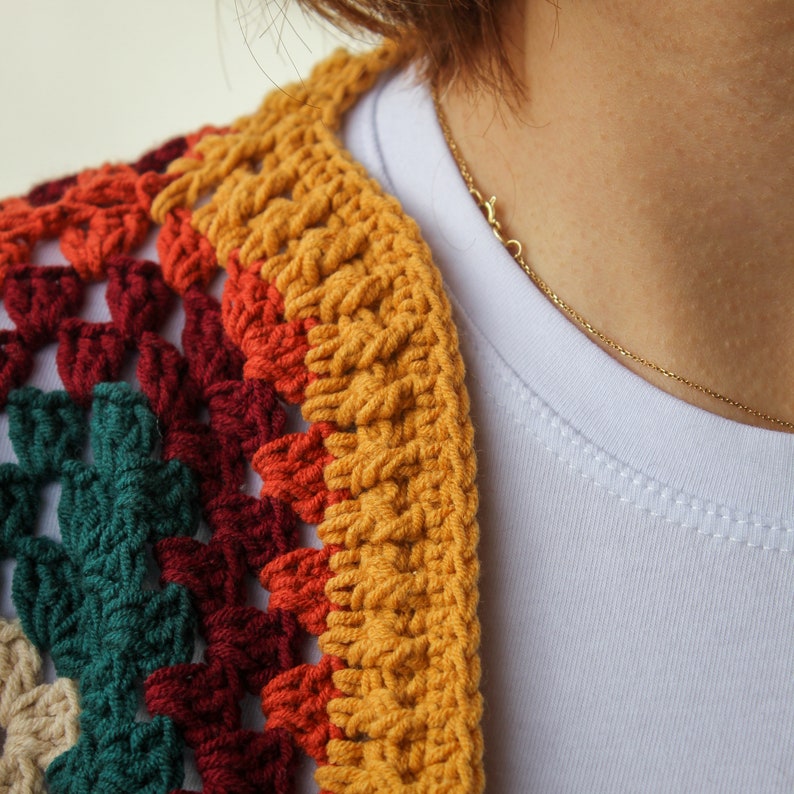 May include: A close-up of a colorful crocheted top with a yellow, orange, red, and green pattern. The top is worn over a white t-shirt with a gold chain necklace.