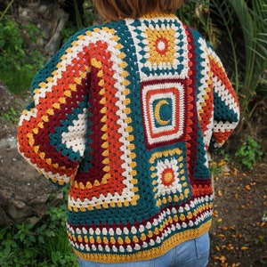 May include: A colorful crocheted cardigan with a geometric pattern in shades of red, orange, yellow, green, and blue. The cardigan is made with a granny square stitch and features a crescent moon design.