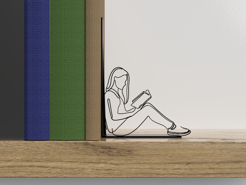 Op de afbeelding: Een zwarte metalen boekenlegger in de vorm van een persoon die zit en een boek leest. De boekenlegger houdt twee boeken vast, een blauwe, een groene en een bruine.