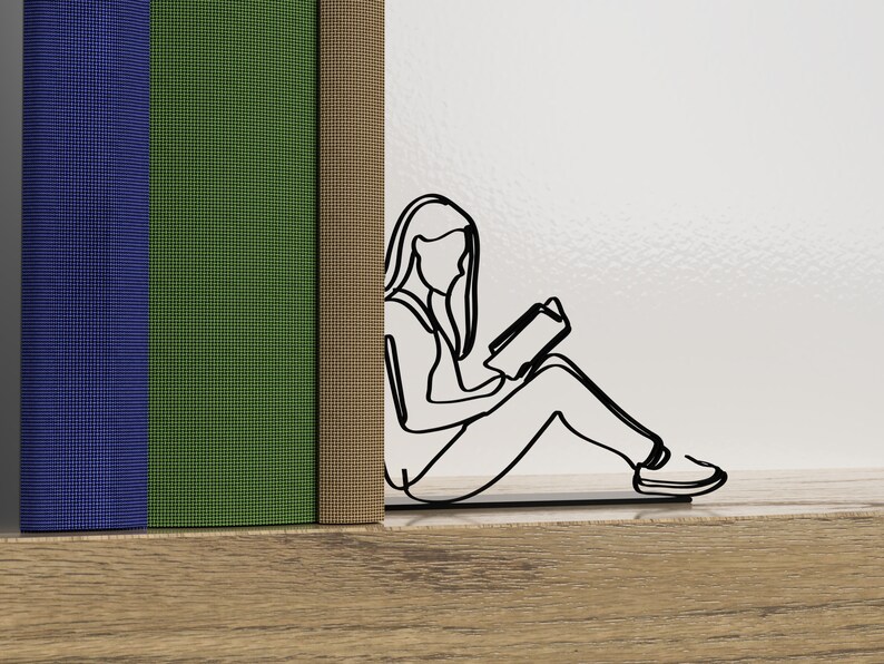 Op de afbeelding: Een zwarte metalen boekenlegger in de vorm van een persoon die zit en een boek leest. De boekenlegger houdt twee boeken vast, een blauwe, een groene en een bruine.