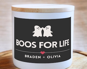 May include: White candle with a black label that says "BOOS FOR LIFE" with two ghost illustrations and the names "BRADEN + OLIVIA" below.