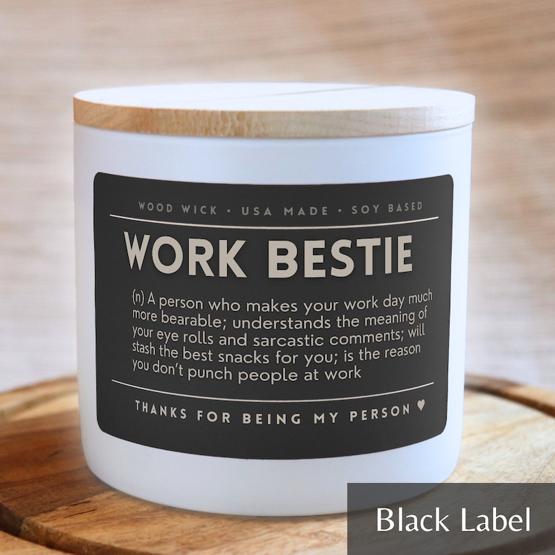 May include: White candle with a black label that reads "Work Bestie" and a definition of the term. The label also says "Wood Wick, USA Made, Soy Based" and "Thanks for being my person".