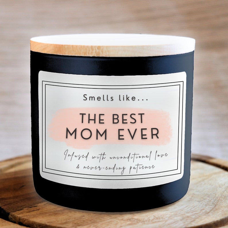 May include: Black candle with a white label that reads "Smells like... THE BEST MOM EVER Infused with unconditional love & never-ending patience".