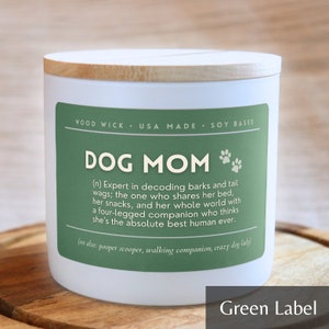 May include: White candle with a green label that reads "DOG MOM (n) Expert in decoding barks and tail wags; the one who shares her bed, her snacks, and her whole world with a four-legged companion who thinks she's the absolute best human ever. (see also: pooper scooper, walking companion, crazy dog lady)"