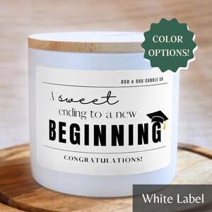May include: White candle with a wooden lid and a label that says "A sweet ending to a new BEGINNING" with a graduation cap graphic. The label also says "CONGRATULATIONS!" and "ASH & OAK CANDLE CO."