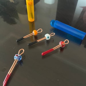 May include: Five colorful glass beads on gold wire with red, orange, blue, and white accents. The beads are attached to a gold wire with a loop at the end. The beads are in a clear plastic container.