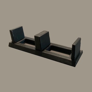 May include: A black 3D printed stand with three slots for holding items. The stand is made of a smooth, matte black plastic.