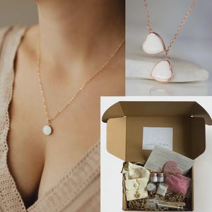 May include: A gold-colored necklace with a small, round, white pendant. Another necklace features two heart-shaped white pendants with a rose gold-colored frame. A brown cardboard box contains a kit with various items, including small jars, a pink cloth, and a necklace.
