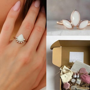 K&ouml;nnte beinhalten: Ein goldener Ring mit einem birnenf&ouml;rmigen wei&szlig;en Stein und kleinen Akzentsteinen. Ein weiterer Ring hat drei wei&szlig;e Steine in Marquiseform. Eine Geschenkbox enth&auml;lt kleine Gegenst&auml;nde, darunter einen Beutel, Gl&auml;ser und einen herzf&ouml;rmigen Artikel.
