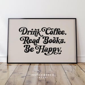 May include: A beige poster with black text that reads "Drink Coffee. Read Books. Be Happy." The poster is framed in a black frame and is sitting on a wooden floor.