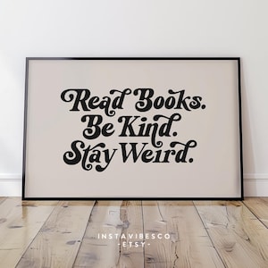 May include: A beige poster with black text that reads "Read Books. Be Kind. Stay Weird." The poster is framed in a black frame and is sitting on a wooden floor.