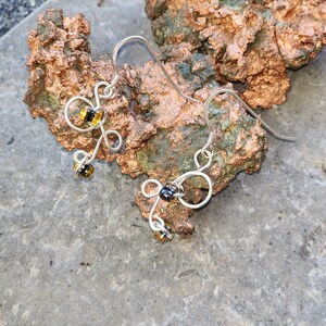May include: A pair of silver wire earrings with black and yellow glass beads. The earrings are shaped like a stylized flower.