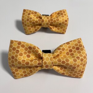 May include: Two brown and yellow bow ties with a honeycomb pattern. The bow ties are made of fabric and have an adjustable strap.