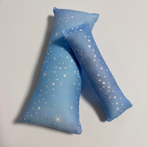 Puede incluir: Dos almohadas azules con un patrón de estrellas blancas. La almohada más grande es rectangular y la almohada más pequeña es un rectángulo largo.