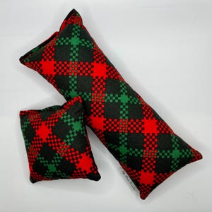 May include: Two plaid pillows, one long and one square, in red, green, and black. The pillows are made of a soft, plush fabric and have a checkered pattern.
