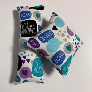 May include: Two white fabric pillows with a blue, purple, and gray pattern. The pillows have the words "XOXO" and "You are amazing" printed on them.