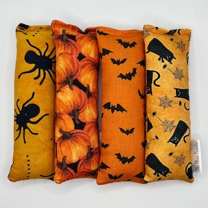 Puede incluir: Cuatro juguetes para gatos con temática de Halloween. Presentan diseños de arañas, calabazas, murciélagos y gatos negros. Los colores son naranja y amarillo, con detalles en negro. El texto "The Three Tuxedos" es visible en uno.