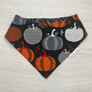 May include: Black bandana with a pattern of orange, grey, and white pumpkins on a black background. The bandana has a small white tag with the text "The Three Twindles".