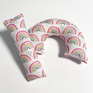 Puede incluir: Dos almohadas suaves y mullidas con forma de arcoíris. Las almohadas son blancas con un patrón de arcoíris rosa, amarillo y azul. Las almohadas tienen puntos negros y corazones.