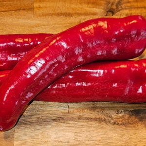 May include: Three red bell peppers on a wooden surface. The peppers are arranged in a stack, with the largest pepper on the bottom and the smallest pepper on top.