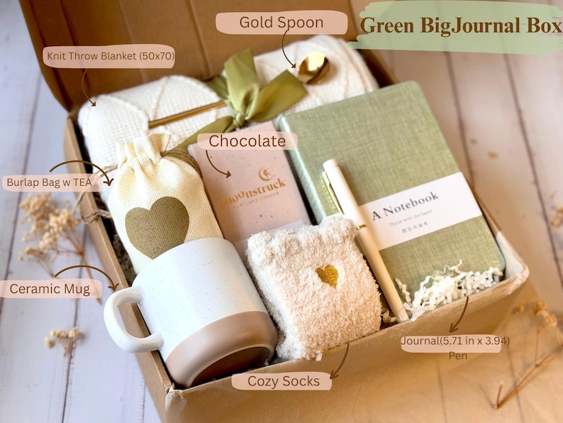 May include: A gift box filled with cozy items, including a knit throw blanket, a ceramic mug, a burlap bag, a bar of chocolate, a journal with a pen, cozy socks, and a gold spoon. The box is decorated with a green ribbon and a gold heart.